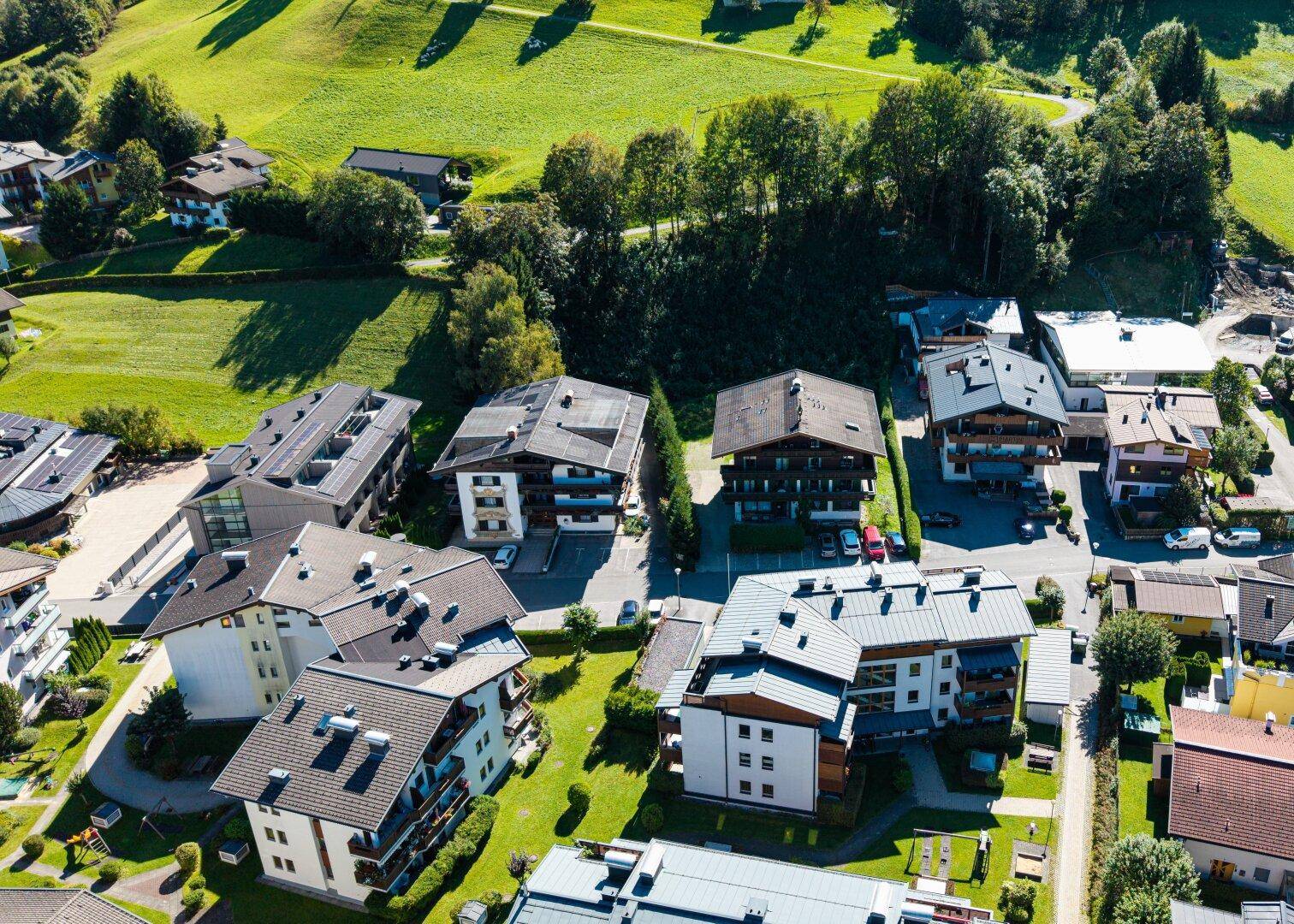 Weitläufige Luftaufnahme einer Siedlung in einem grünen Tal, umgeben von bewaldeten Hügeln und Wiesen.