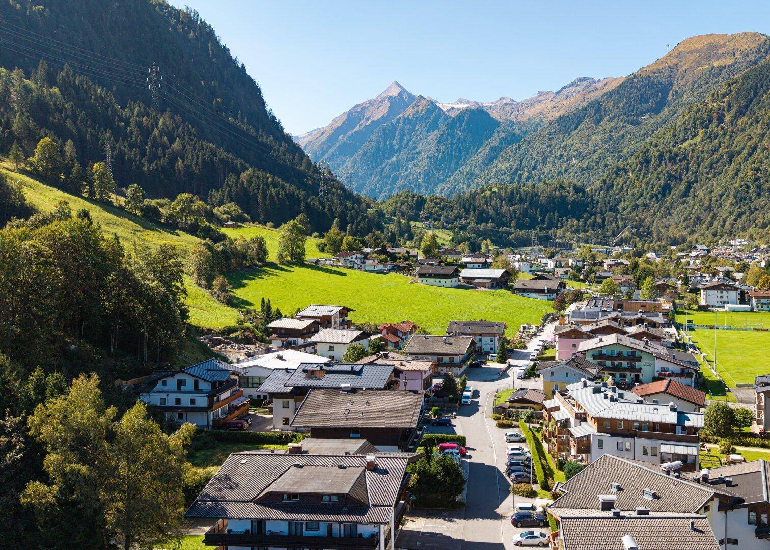 Beeindruckende Panoramaaufnahme eines malerischen Tals mit einem Dorf, umgeben von majestätischen Bergen und Wäldern.