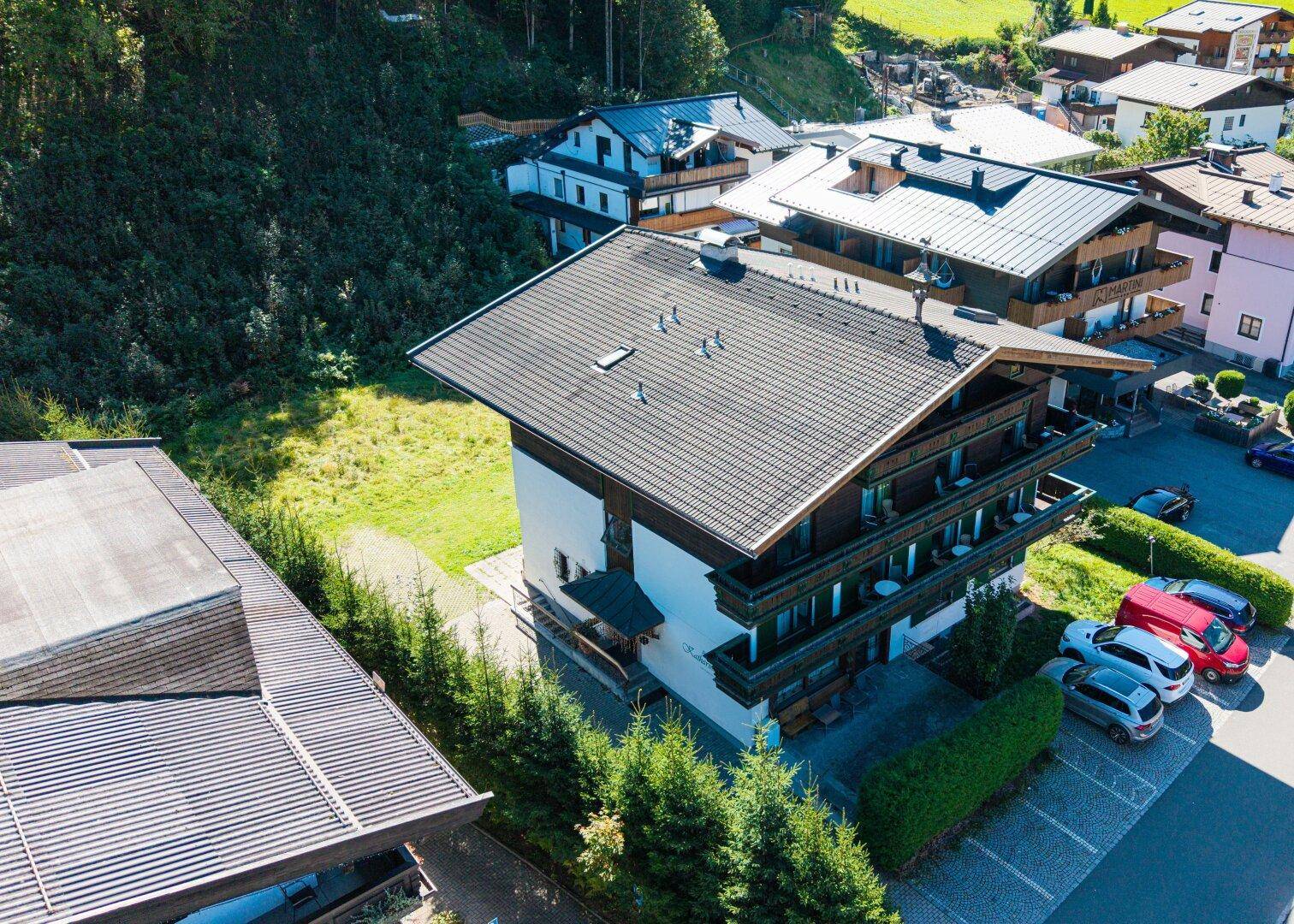 Luftaufnahme eines Gebäudes mit traditioneller Holzfassade und Satteldach, umgeben von Bäumen und einer Grünfläche.