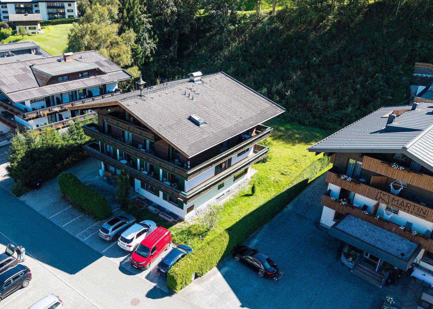 Vogelperspektive eines traditionellen Mehrfamilienhauses mit mehreren Balkonen und angrenzenden Parkmöglichkeiten.