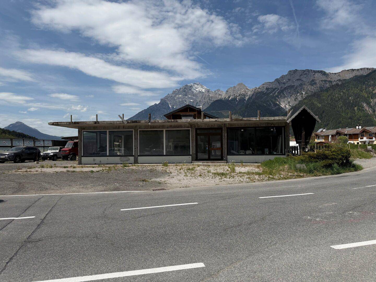Gebäude im Rohbau mit großen Fensterfronten und Bergblick, gelegen an einer Straße in alpiner Umgebung.