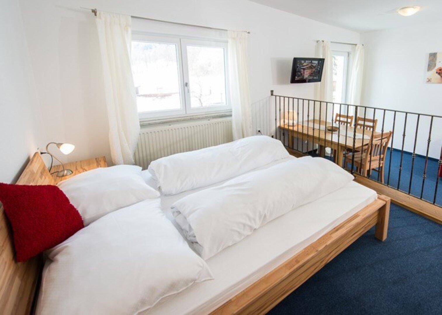 Schlafzimmer mit Doppelbett und Blick auf einen tiefer gelegenen Essbereich, getrennt durch ein Geländer.