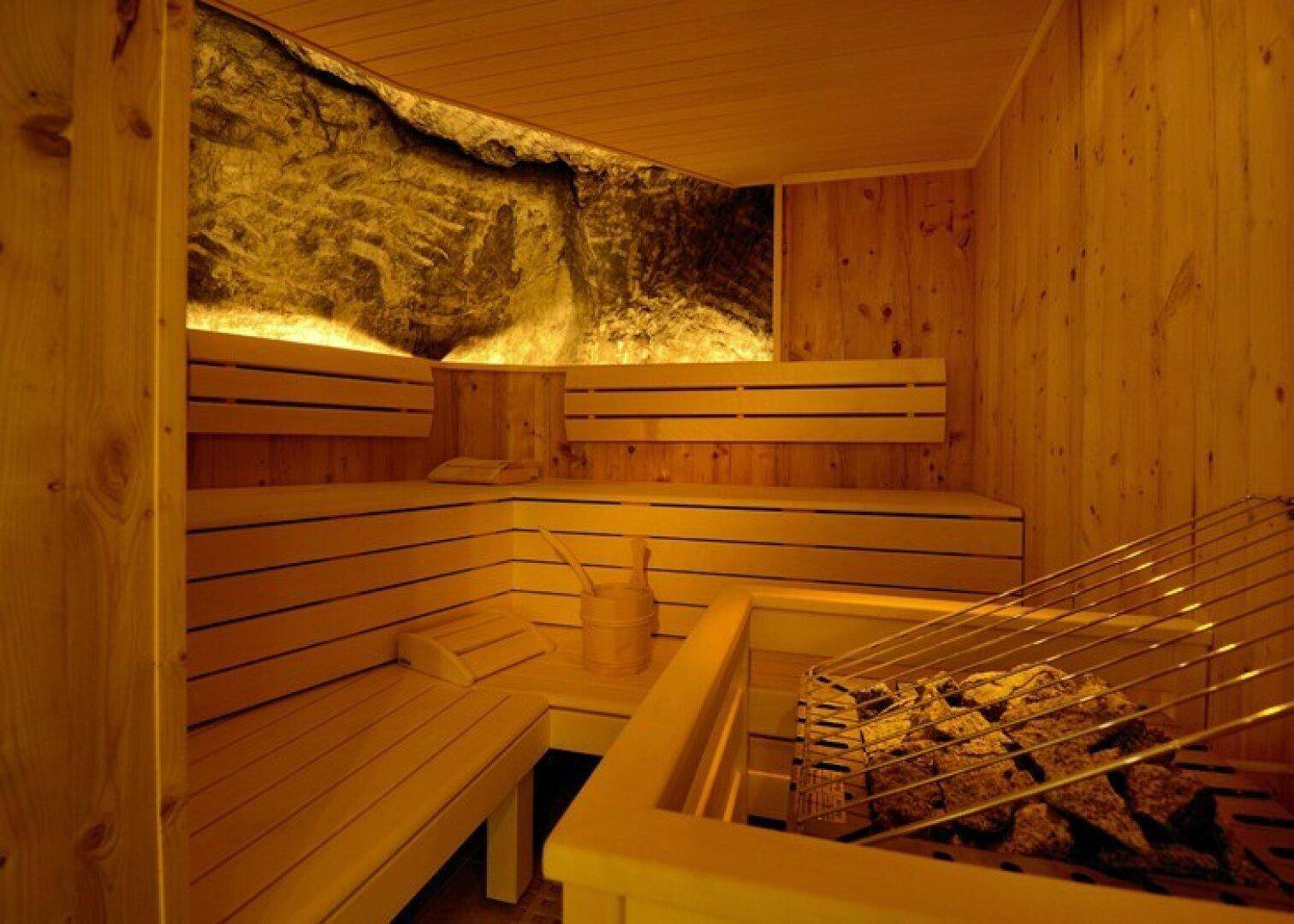 Traditionelle Sauna mit Holzverkleidung, mehrstufigen Bänken und einer markanten Steinwand als Akzent.