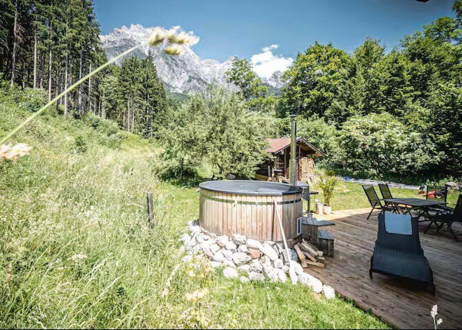 Holzterrasse mit Whirlpool und Sitzbereich, umgeben von Natur und Bergblick.