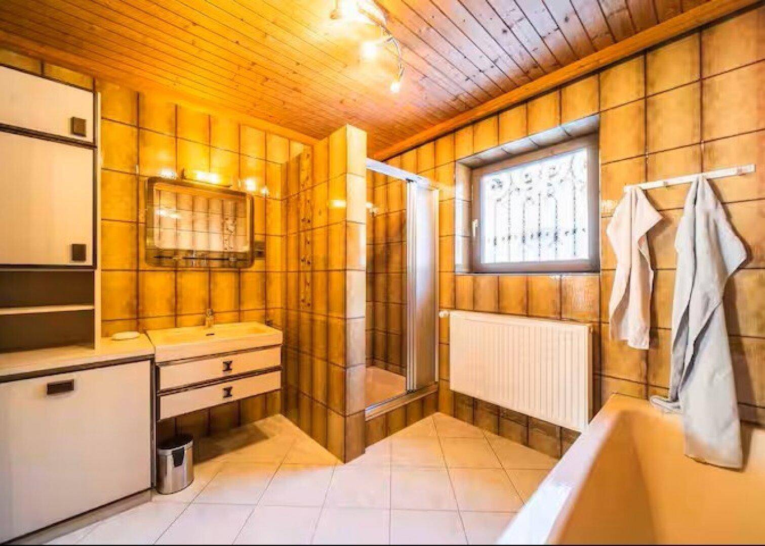 Badezimmer im 80er-Jahre-Stil mit gelben Fliesen, Dusche und Badewanne.