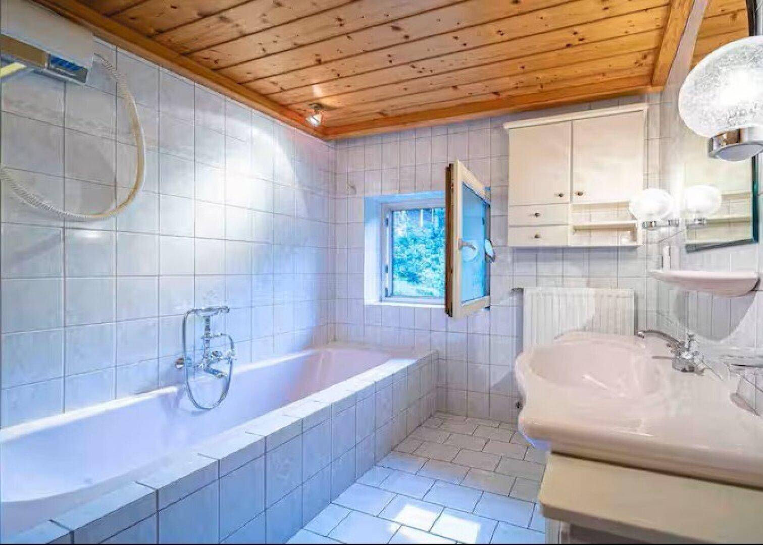 Helles Badezimmer mit Badewanne, Fliesen und Holzdecke.