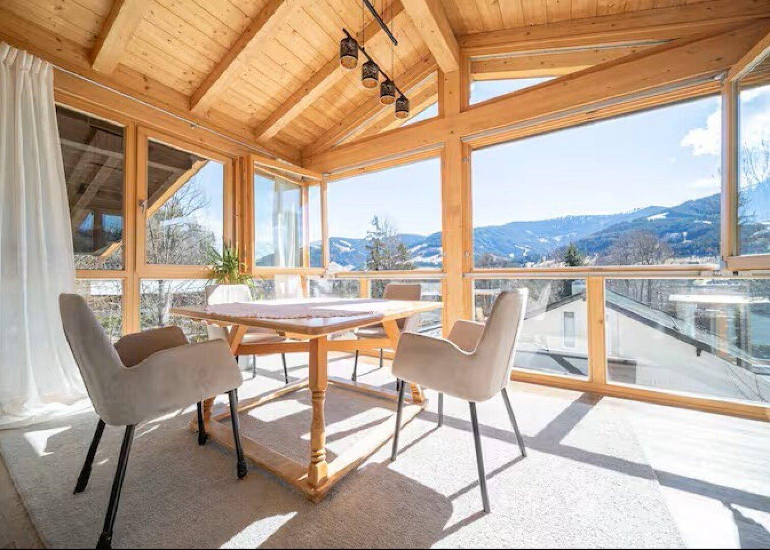 Heller Wintergarten mit Holzbalken und großen Fenstern, die einen weiten Blick bieten.