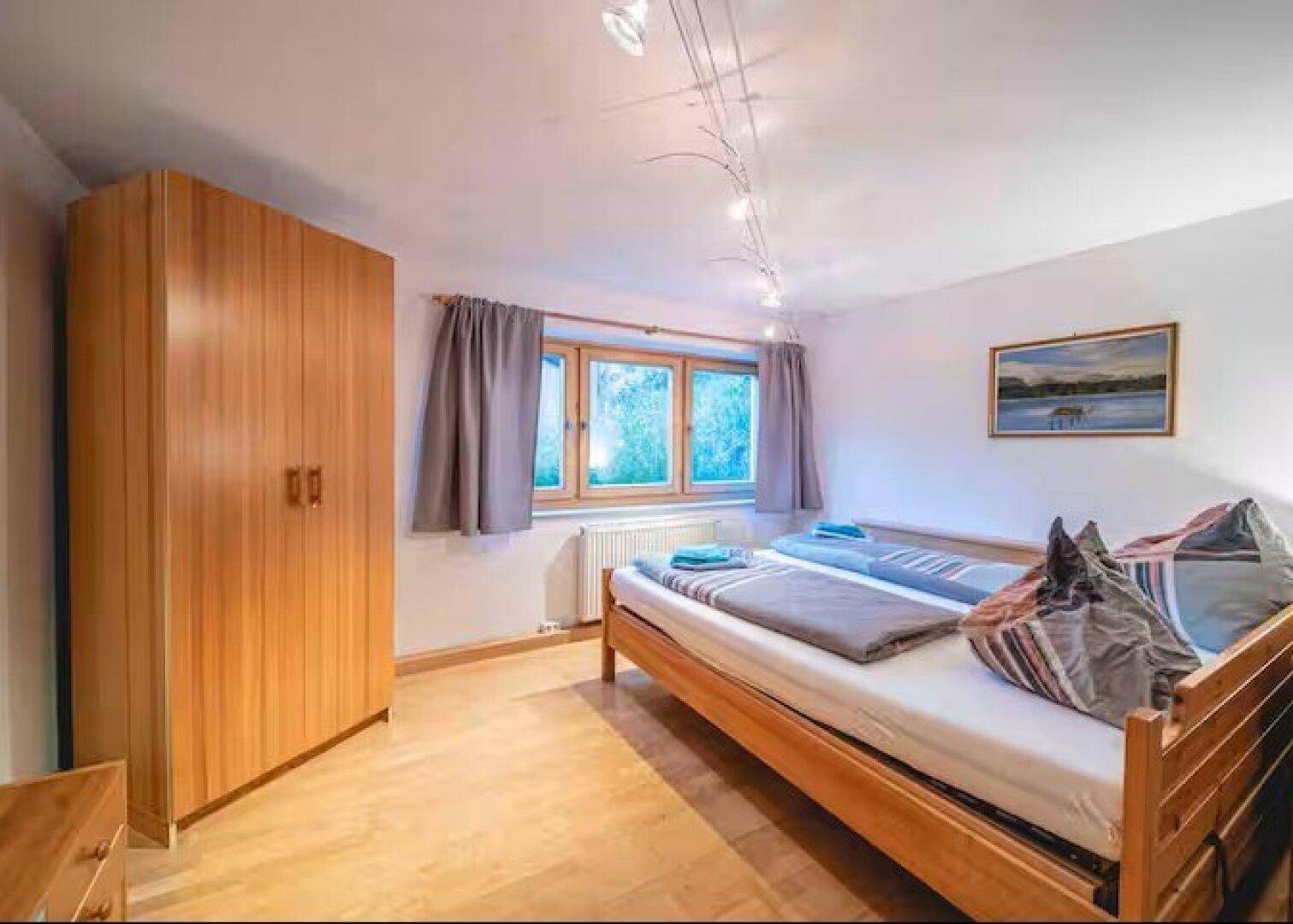 Helles Schlafzimmer mit Holzboden, Kleiderschrank und Blick ins Grüne.