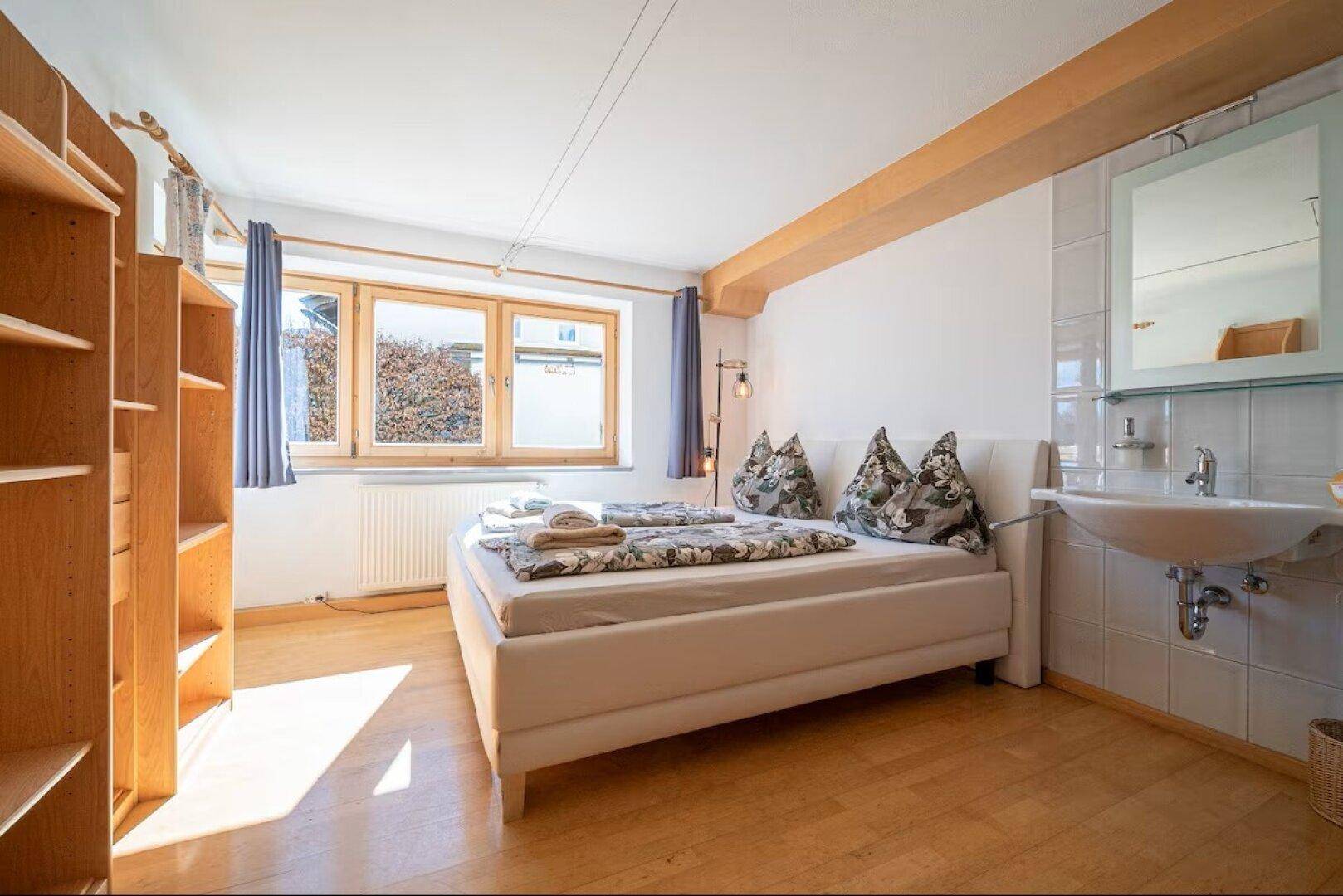 Schlafzimmer mit integriertem Waschbecken, Holzboden und hellen Wänden.