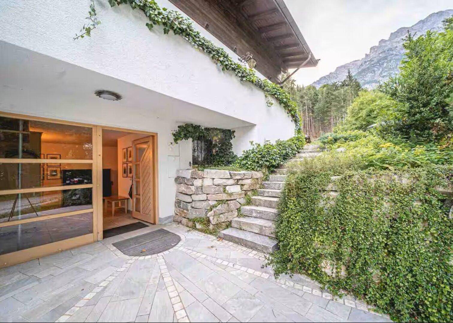 Eingangsbereich mit Steintreppe und üppiger Begrünung, die zum Haus hinaufführt.