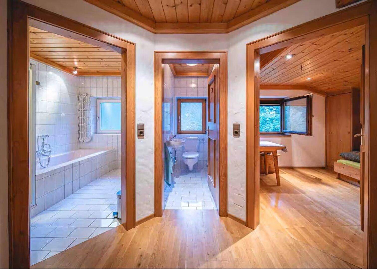 Flur mit Holzboden und Zugang zu Badezimmer, WC und einem weiteren Raum.