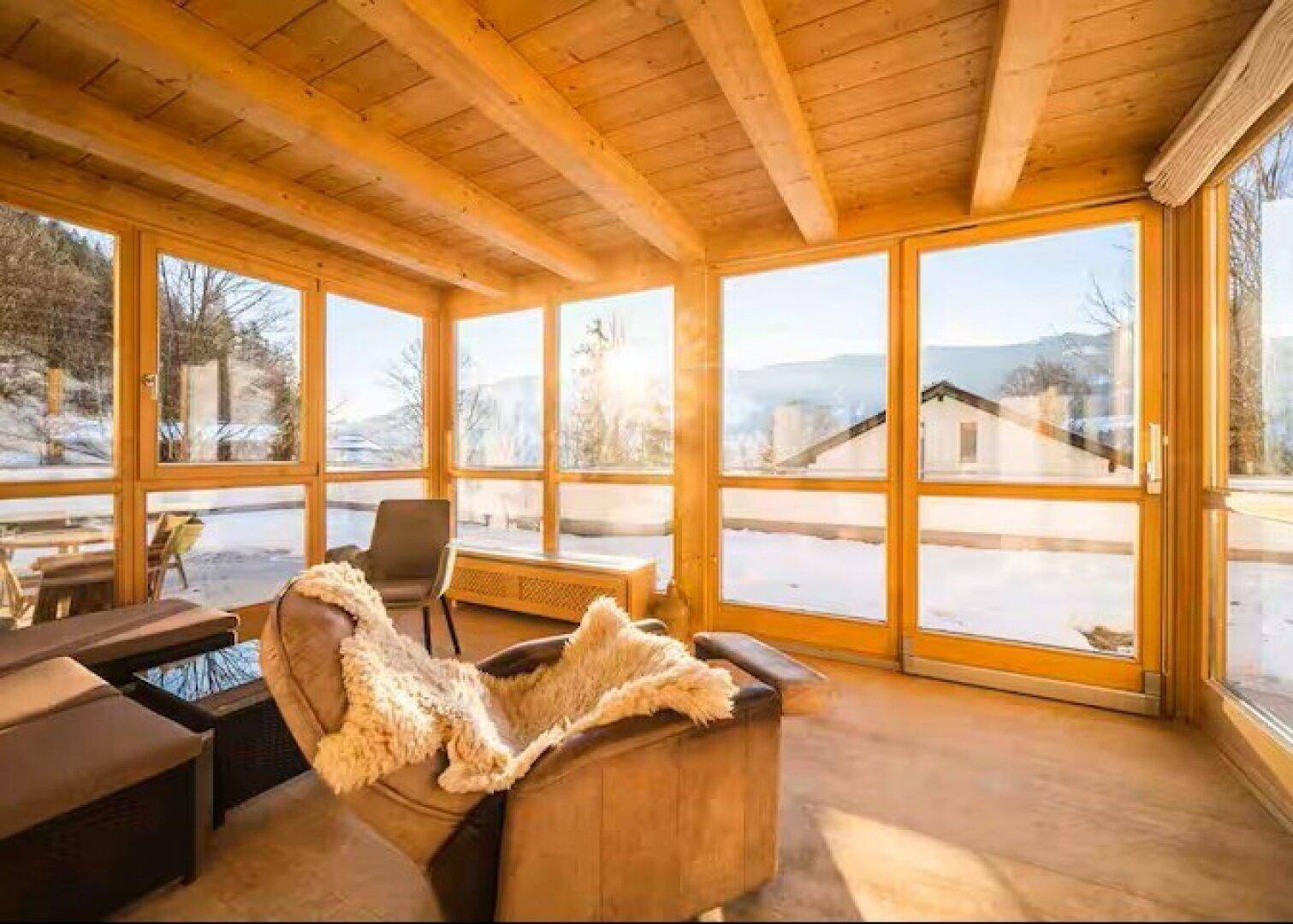 Sonniger Wintergarten mit Holzboden und Panoramablick auf die verschneite Landschaft.