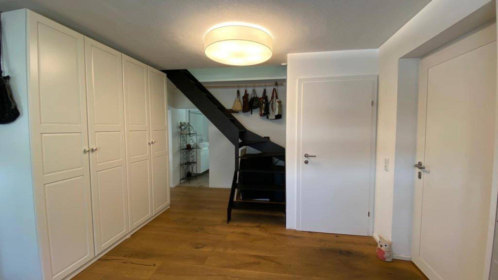 Heller Flur mit weißen Einbauschränken, moderner schwarzer Treppe und Holzboden.
