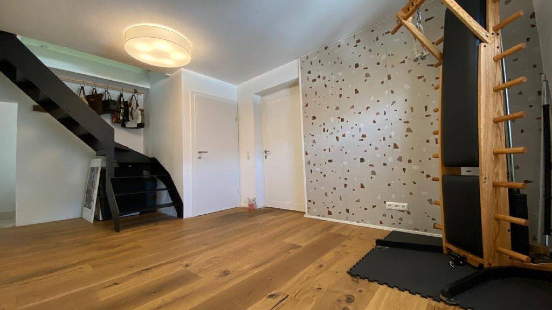 Geräumiger Flur mit gemusterter Wand, Holzboden und integriertem Fitnessbereich.