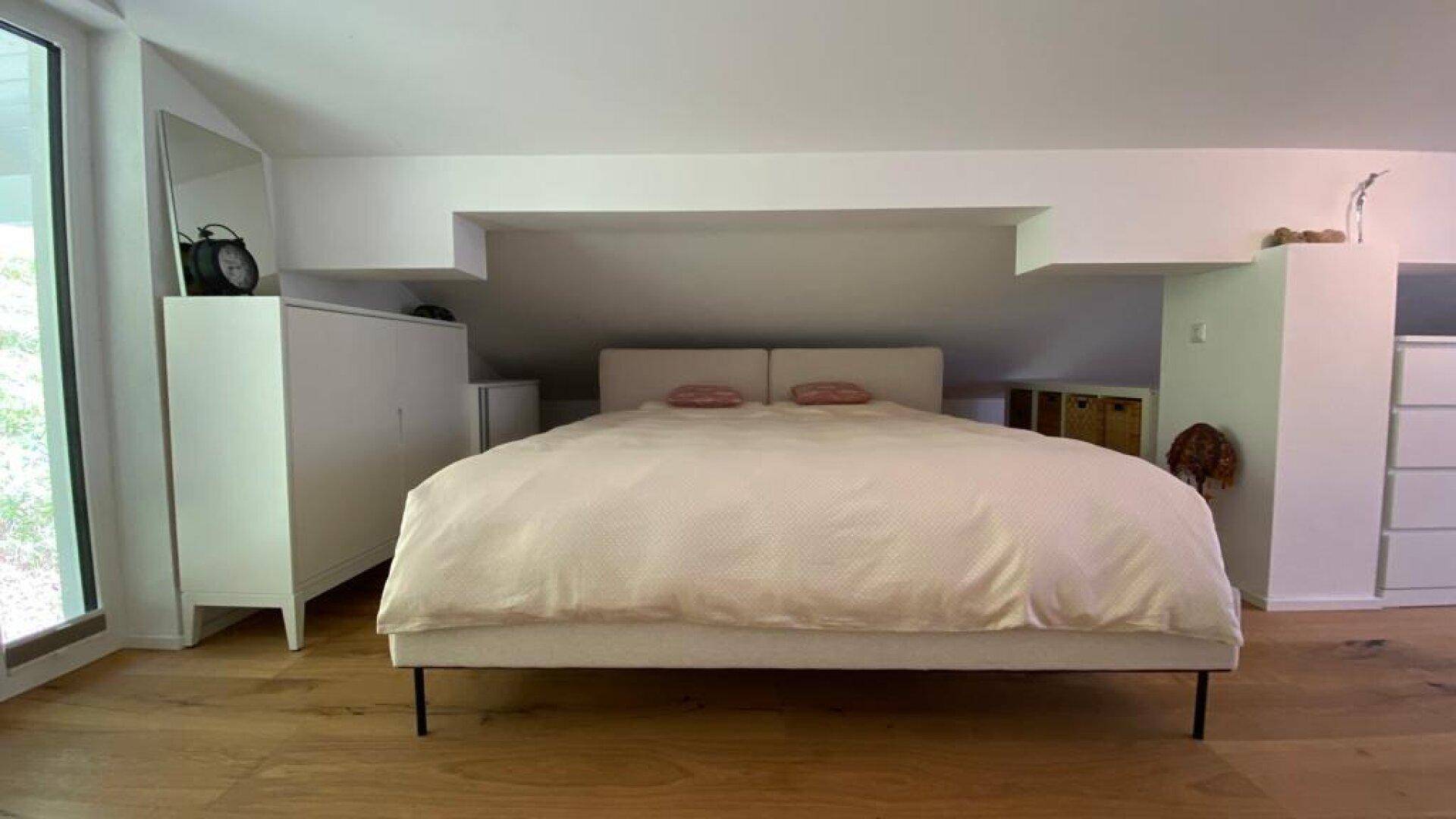 Schlafzimmer im Dachgeschoss mit großem Bett, Holzboden und viel natürlichem Licht.