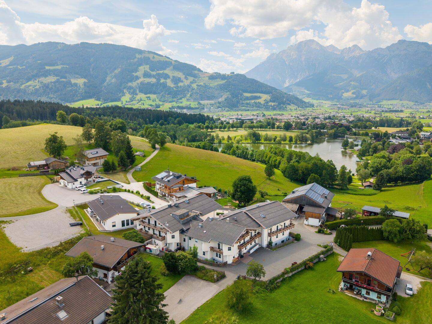 Panoramablick auf die gesamte Anlage mit mehreren Gebäuden, See und majestätischem Bergblick.