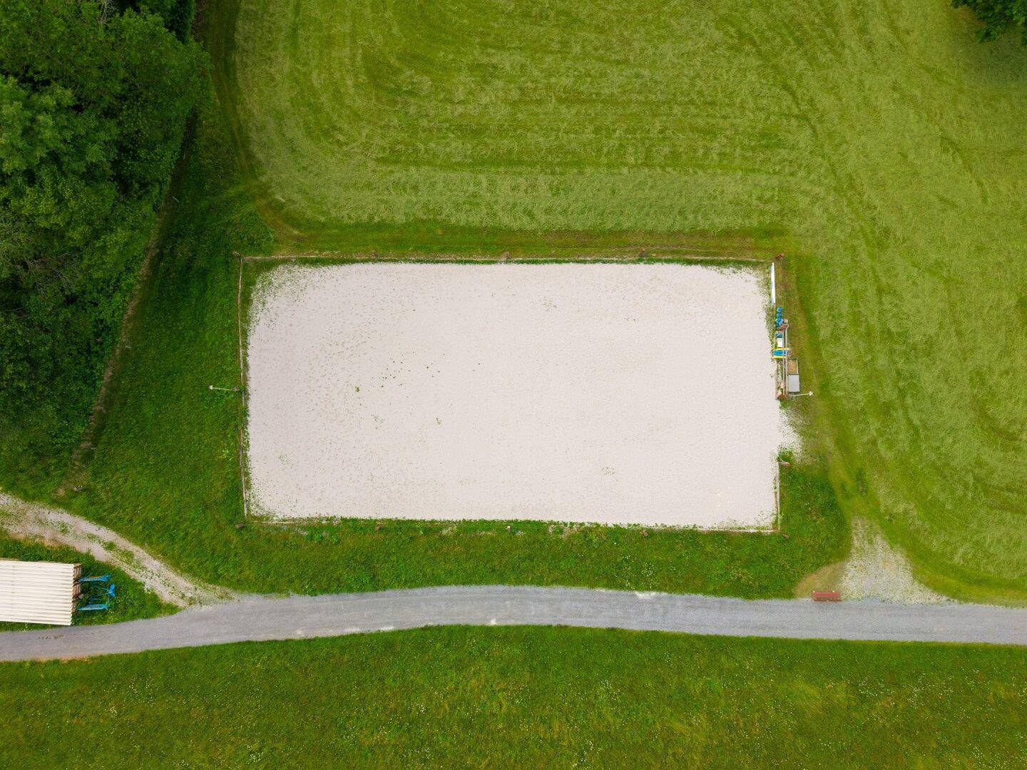 Luftaufnahme eines rechteckigen Reitplatzes, umgeben von grünen Wiesen.