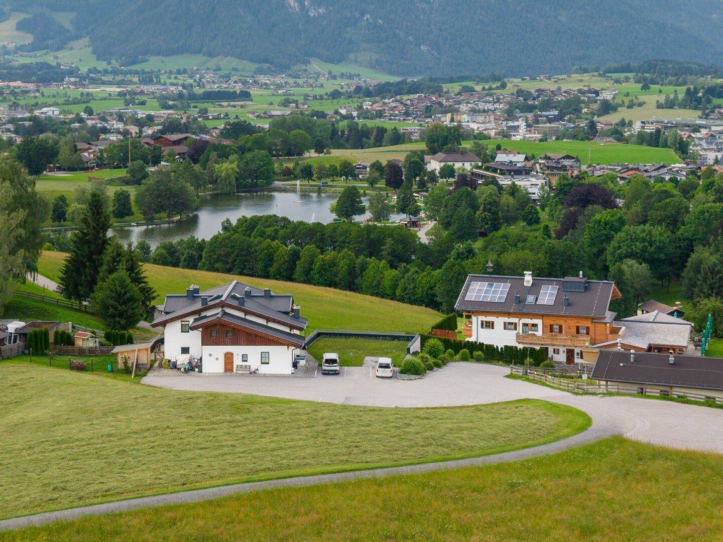 Weitläufige Landschaft mit mehreren Gebäuden, einem See und Bergblick unter blauem Himmel.