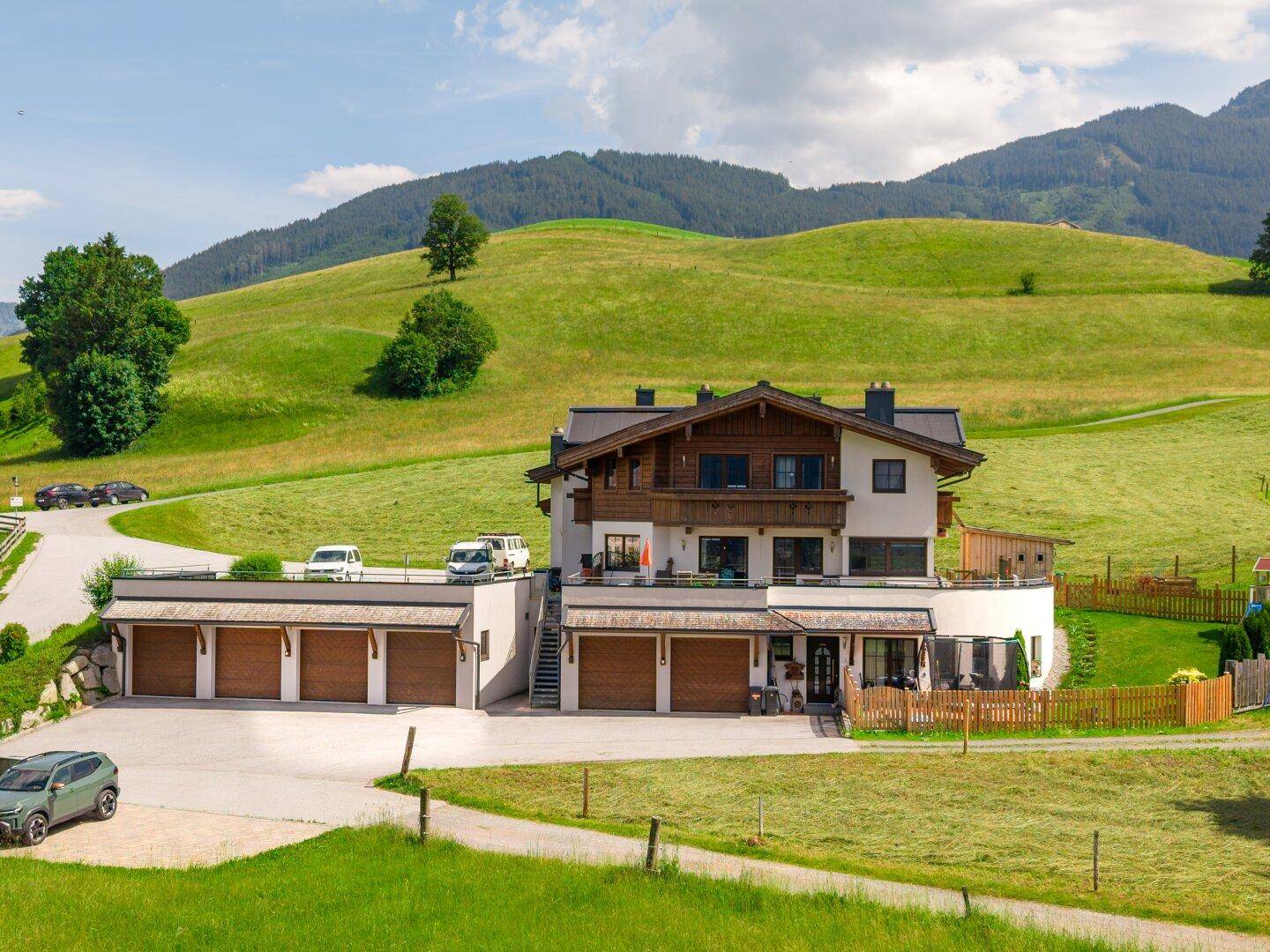 Modernes Gebäude mit Garagen und einer Terrasse, umgeben von grünen Hügeln.