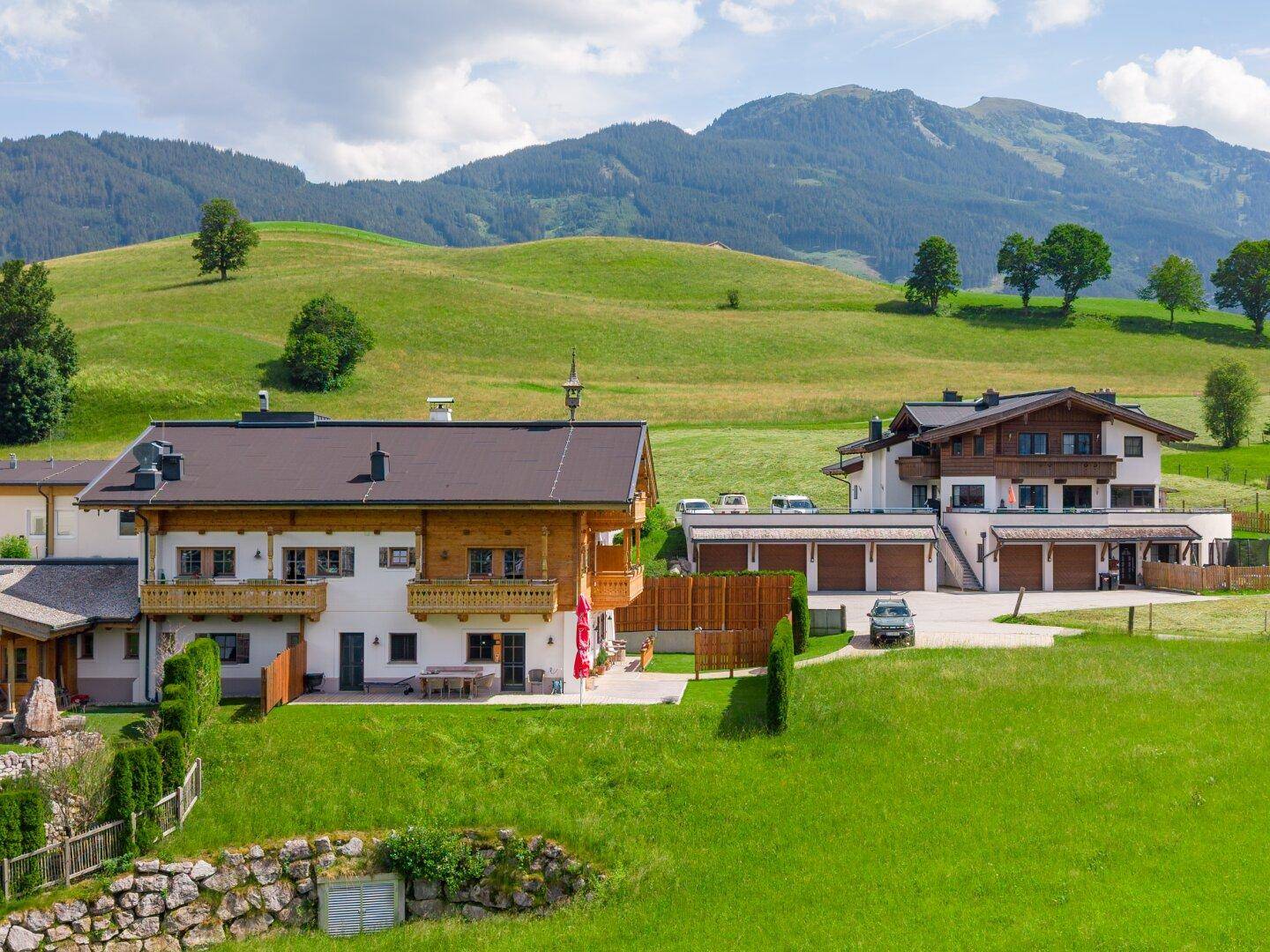 Zwei Gebäude im alpinen Stil eingebettet in die grüne Hügellandschaft mit Bergblick.