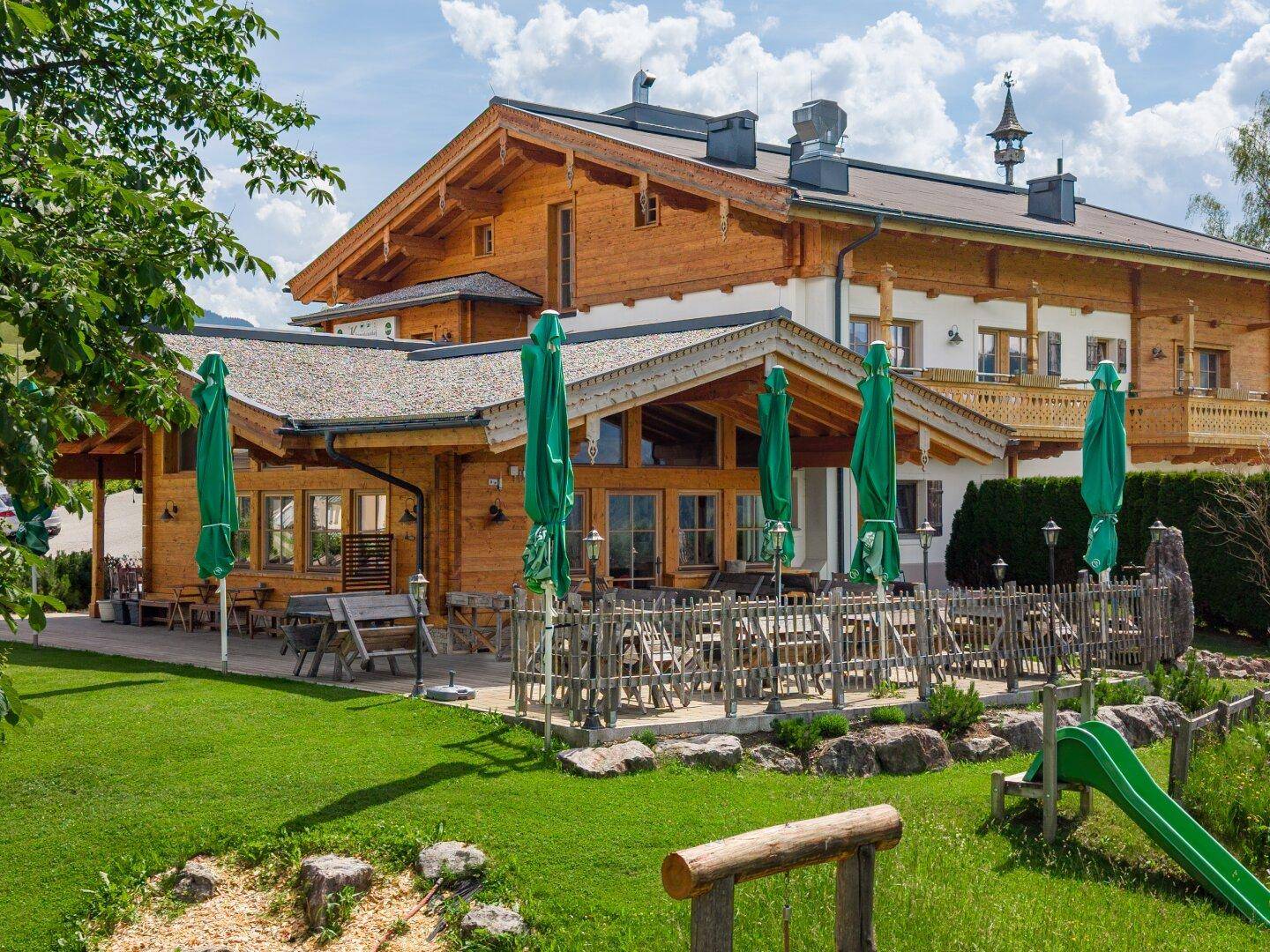 Gemütliche Außenterrasse mit Sonnenschirmen und angrenzendem Kinderspielplatz.