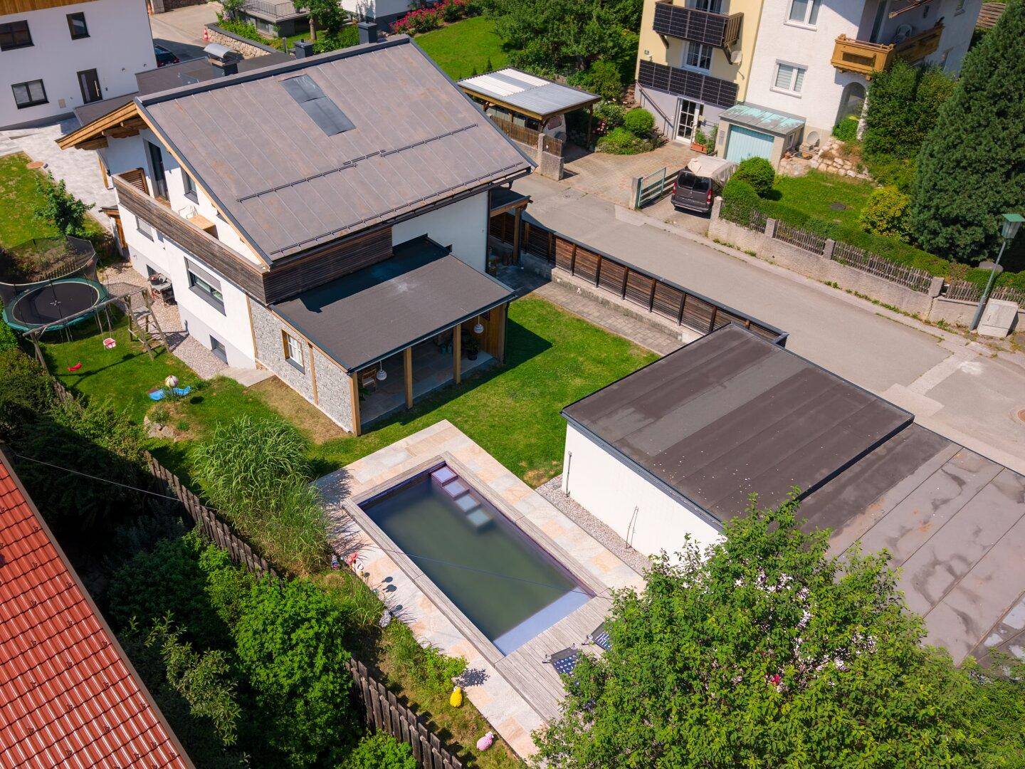 Vogelperspektive des Anwesens mit Pool, Garten, Garage und umliegender Bebauung, sonnig gelegen.