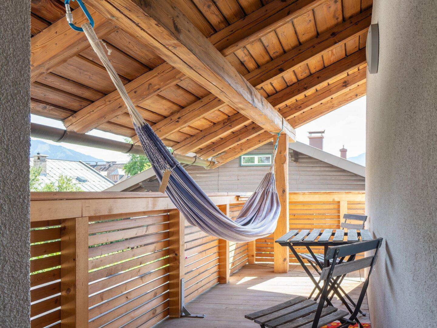 Überdachter Balkon mit Holzboden, Hängematte und Sitzgelegenheiten, ideal zum Entspannen.