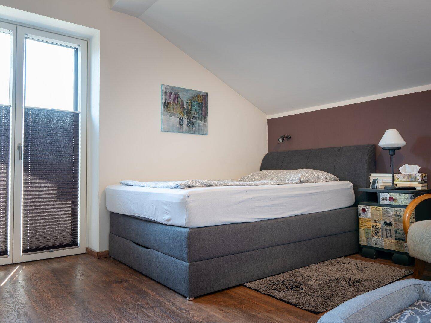Schlafzimmer im Dachgeschoss mit Holzboden, schräger Decke und großem Fenster, hell und gemütlich.