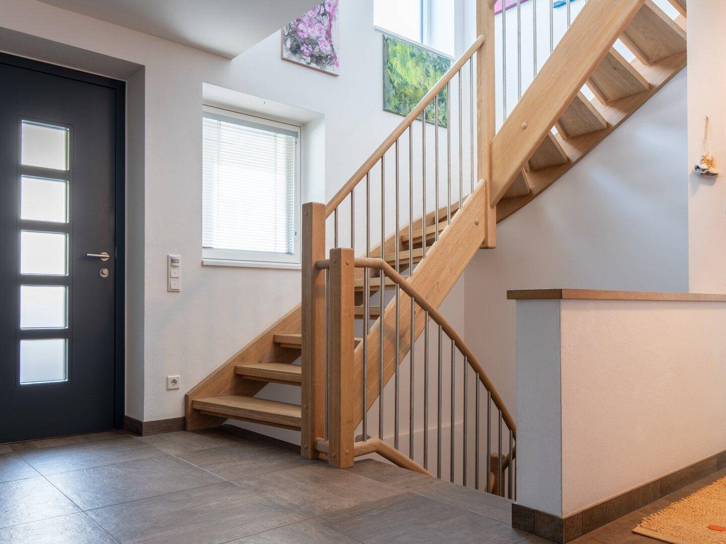 Heller Eingangsbereich mit moderner Holztreppe und Fliesenboden, einladend und geräumig.