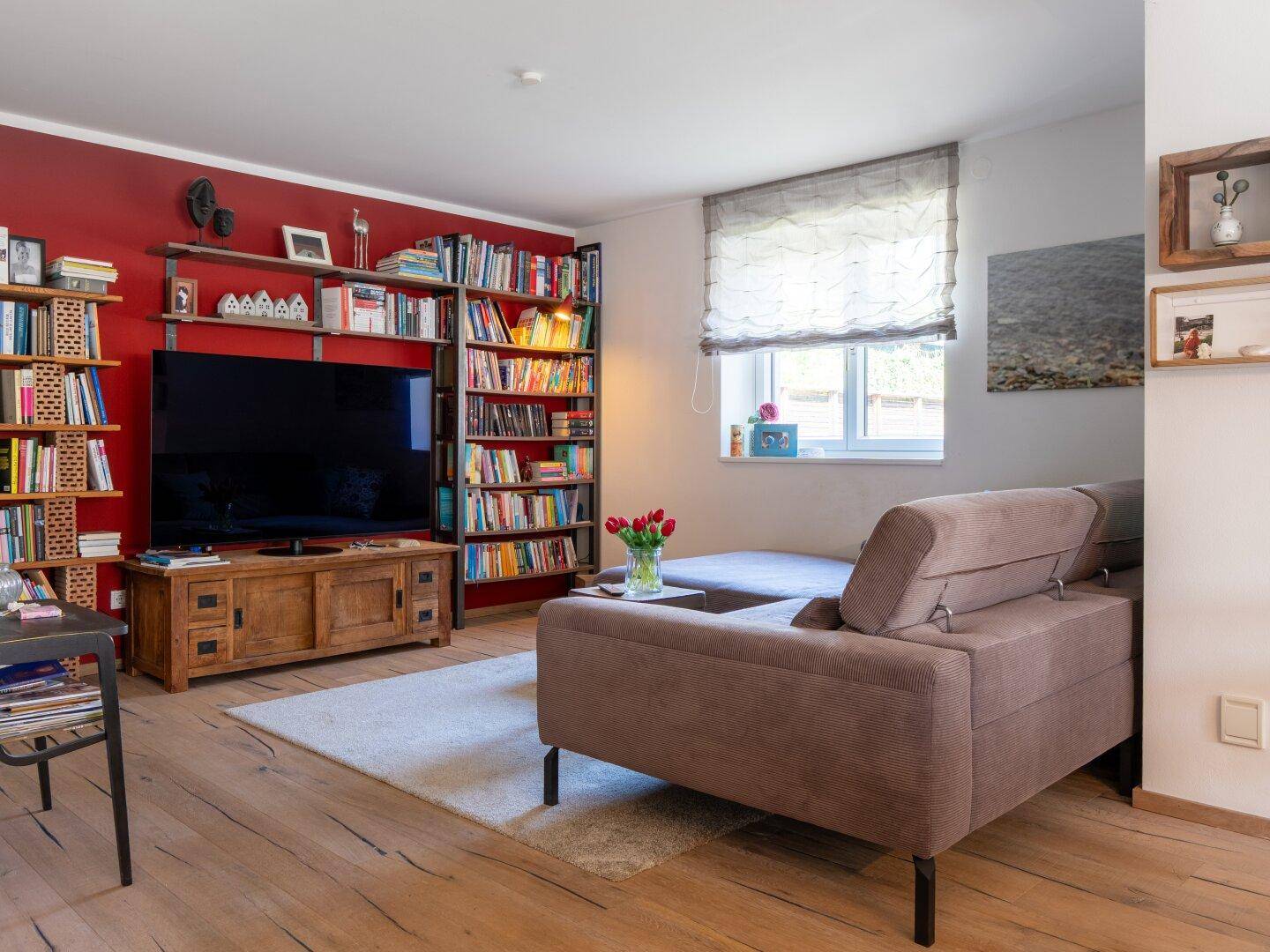 Gemütliches Wohnzimmer mit roter Akzentwand, Bücherregalen und bequemer Couch, einladend und hell.