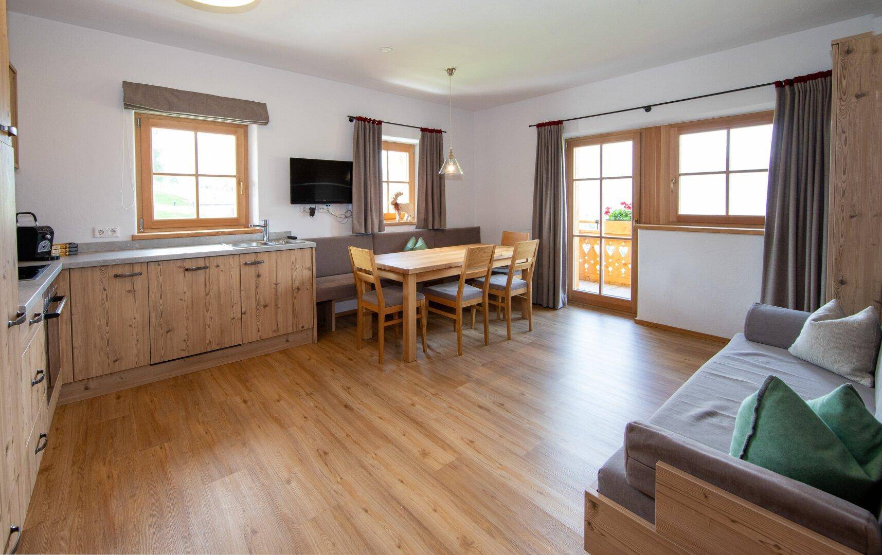 Heller Wohn-Essbereich mit integrierter Küchenzeile, Holzboden und Zugang zum Balkon.