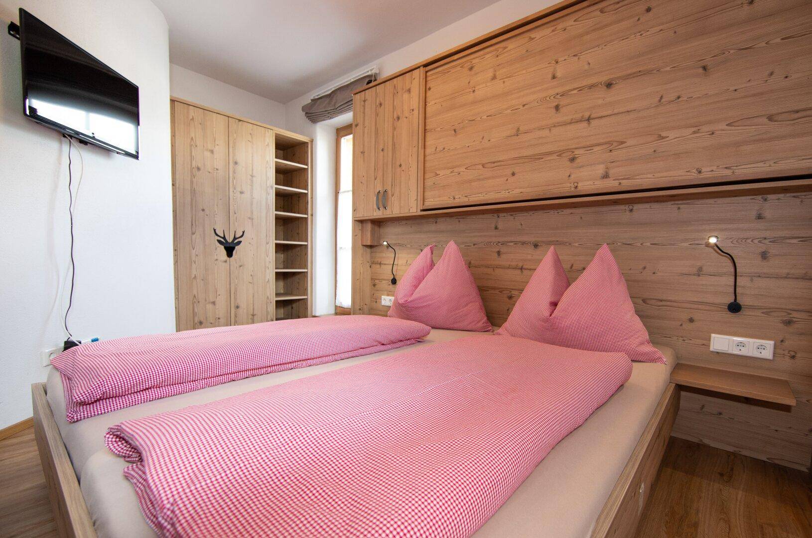 Schlafzimmer mit Holzeinrichtung, zwei Betten und einem an der Wand montierten Fernseher.