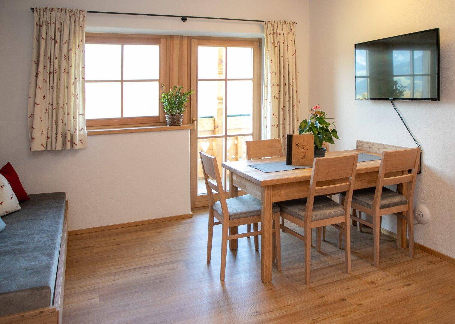 Gemütlicher Essbereich mit Holztisch und Stühlen, direkt neben einem Sofa und mit Zugang zum Balkon.