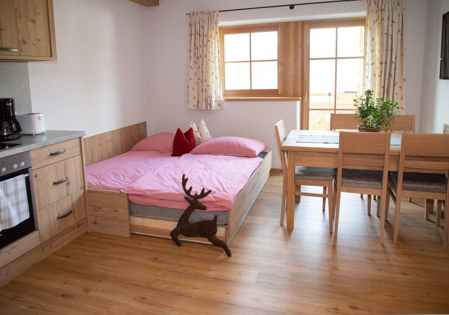 Flexibler Wohnraum mit ausziehbarem Bett, Essbereich und kleiner Küchenzeile.