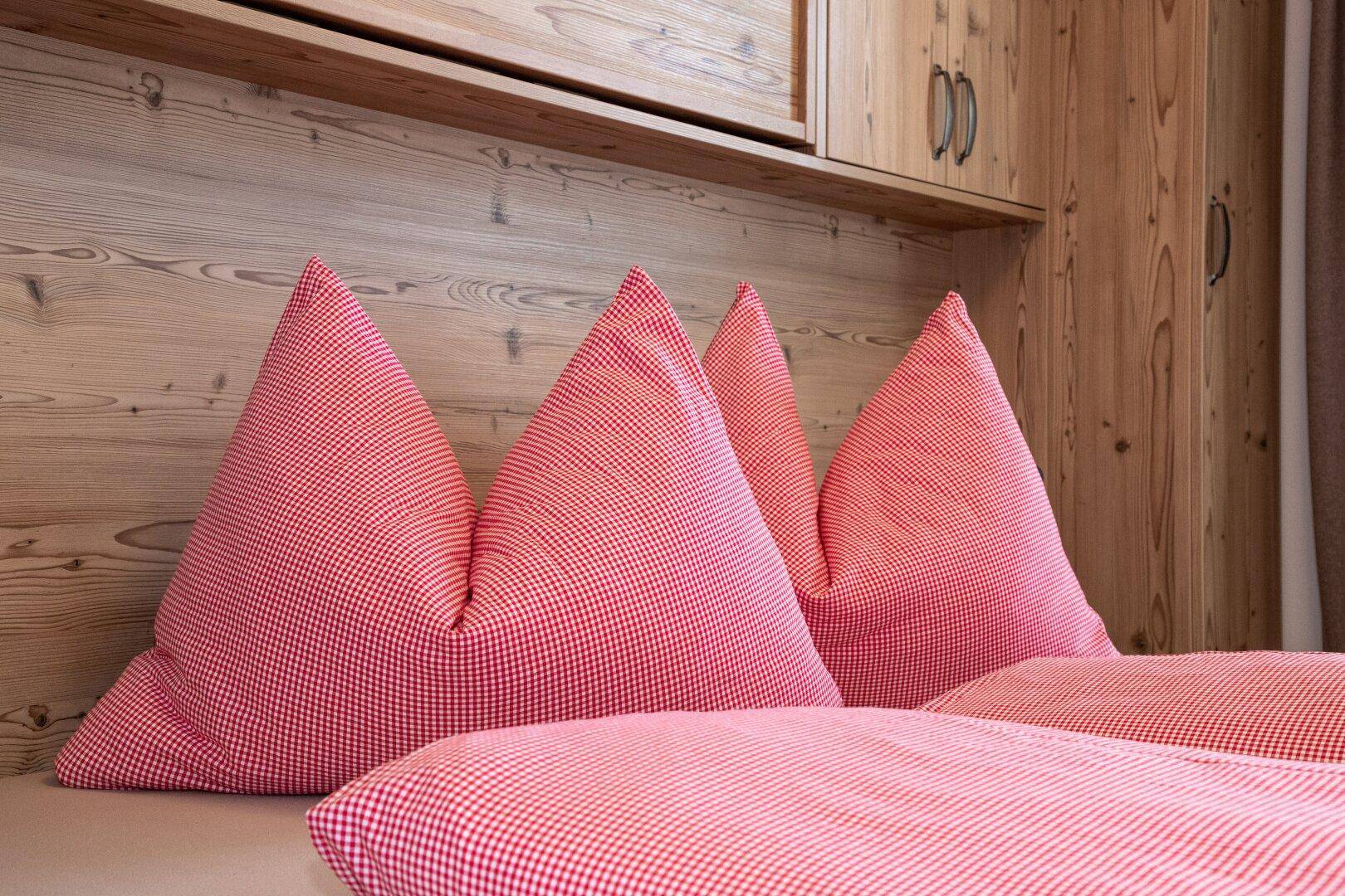 Nahaufnahme von karierten Kissen und Bettwäsche auf einem Holzbett in einem Schlafzimmer.