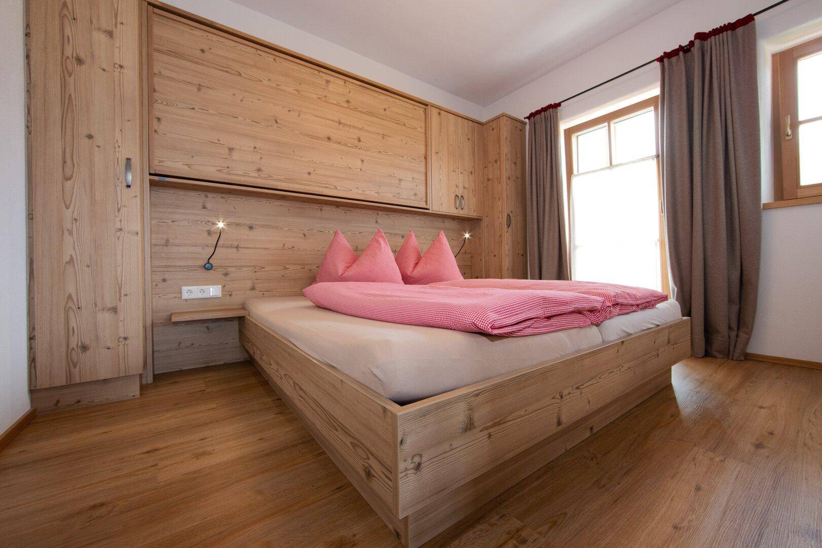 Schlafzimmer mit hellem Holzbett, integrierten Schränken und Zugang zum Balkon.