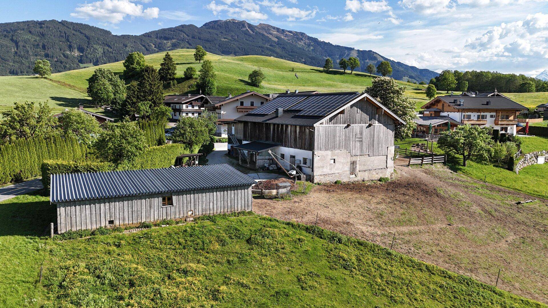 Ländliche Gebäude mit Holzbalken und Wellblechdächern inmitten grüner Hügel.