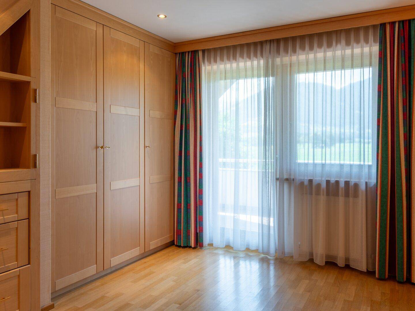 Schlafzimmer mit Einbauschränken, Holzboden und großem Fenster mit Bergblick.