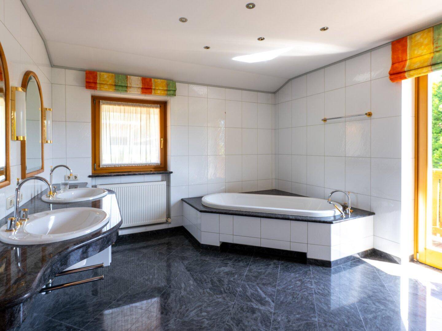 Großes Badezimmer mit Doppelwaschbecken, Eckbadewanne und Zugang zum Balkon.