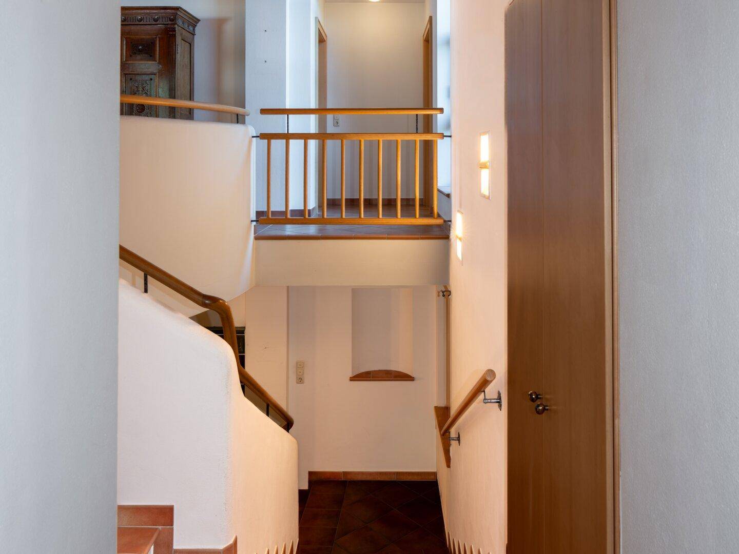 Treppenhaus mit Holzgeländer, Terrakottafliesen und mehreren Ebenen.