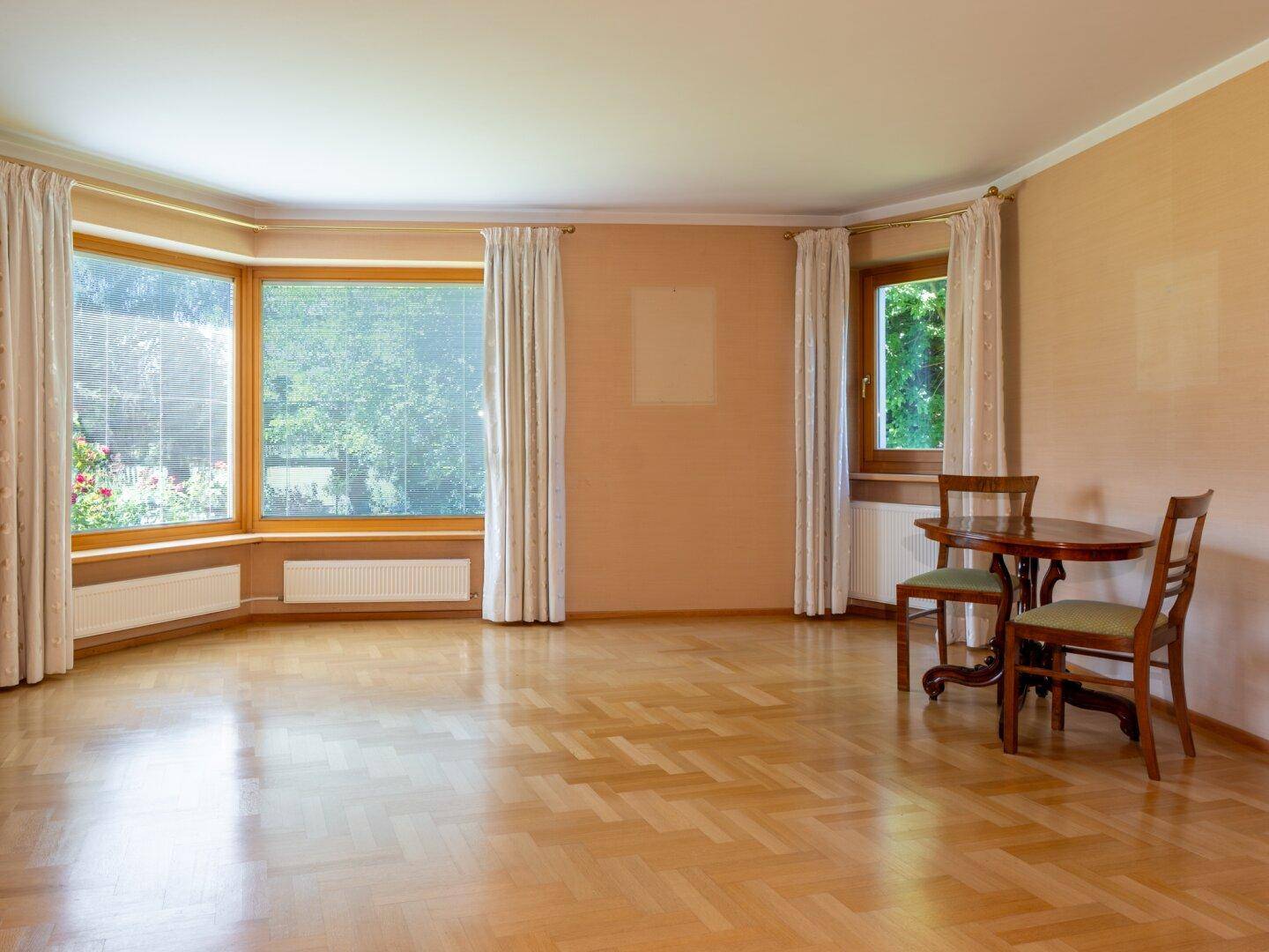 Helles Wohnzimmer mit Parkettboden, großen Fenstern und Blick ins Grüne.