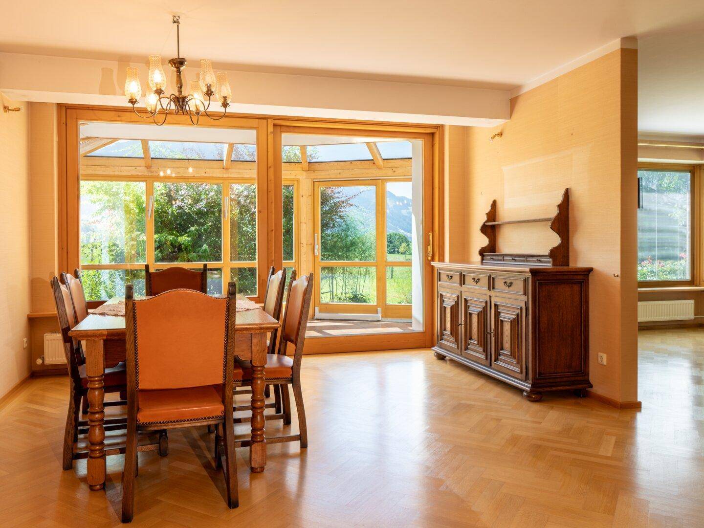 Gemütlicher Essbereich mit Holztisch, Stühlen und Zugang zum Wintergarten mit Bergblick.