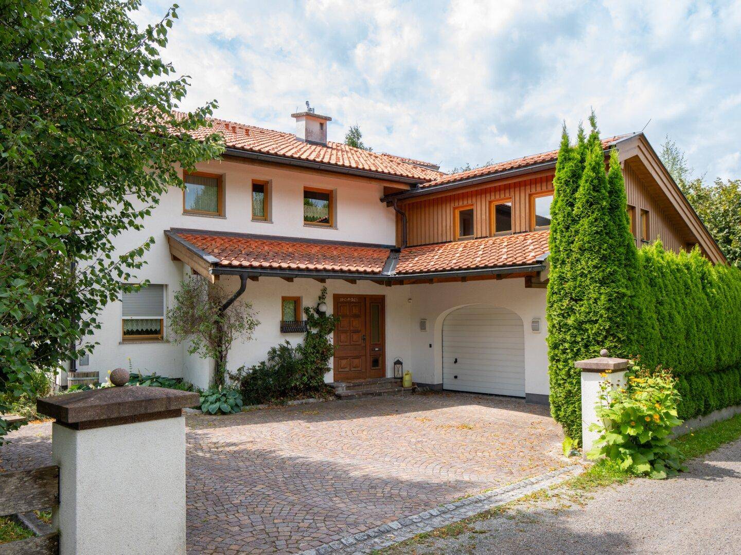 Eingangsbereich des Hauses mit gepflasterter Auffahrt, Garage und gepflegter Hecke.