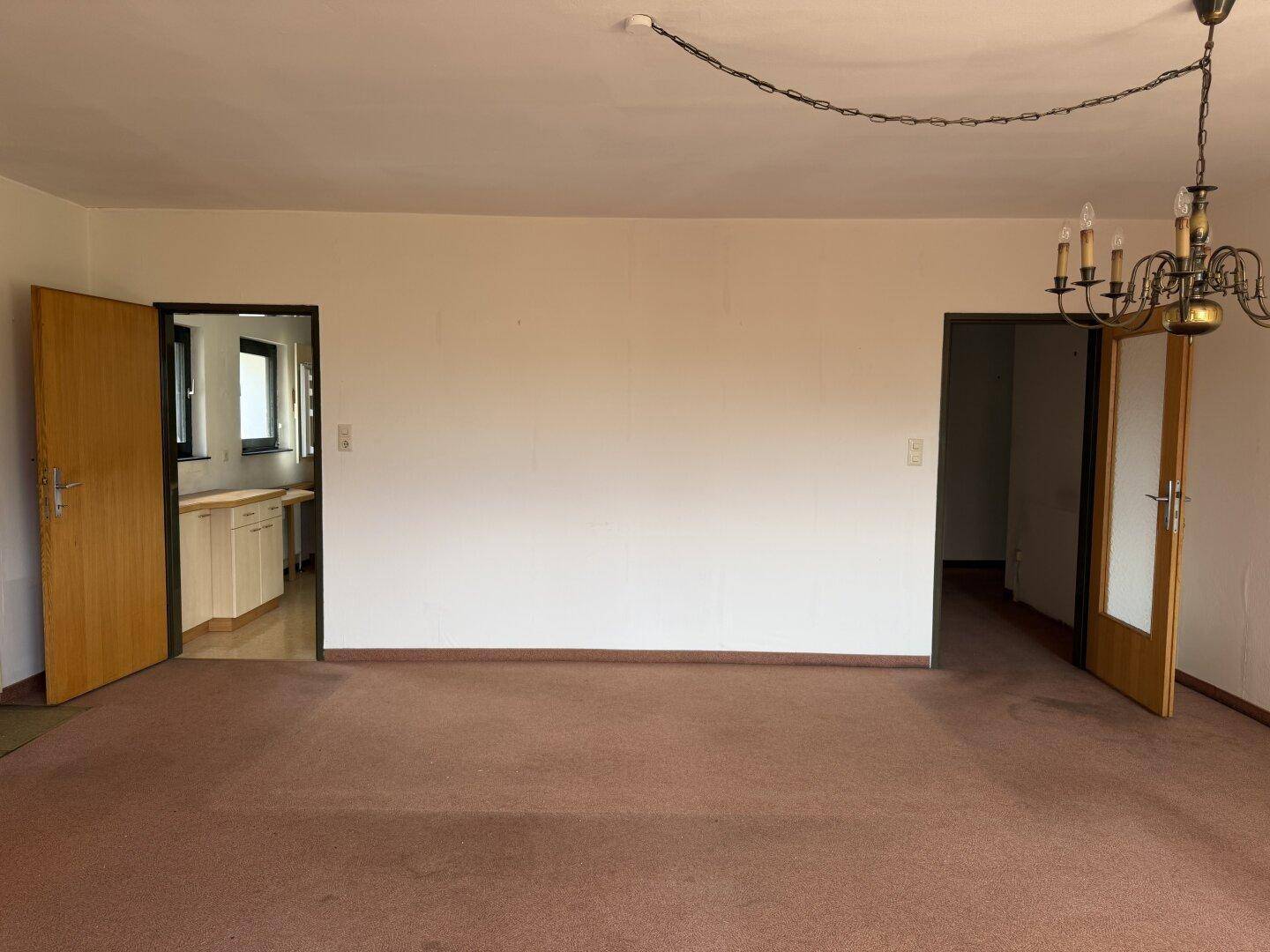 Heller Raum mit Teppichboden und zwei offenen Türen, die zu weiteren Zimmern führen.