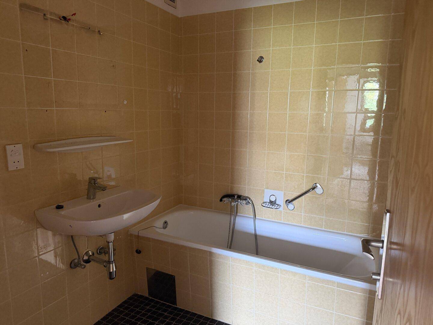 Badezimmer mit gelben Fliesen, Badewanne, Waschbecken und Haltegriffen für mehr Sicherheit.