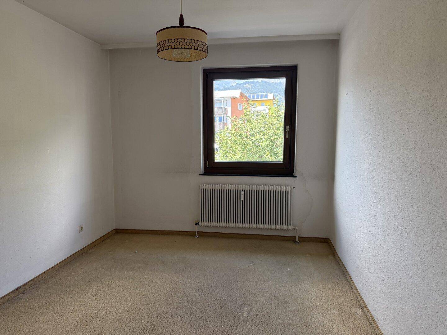 Helles Zimmer mit Teppichboden, einem Fenster und einem Heizkörper, ideal als Schlaf- oder Arbeitszimmer.