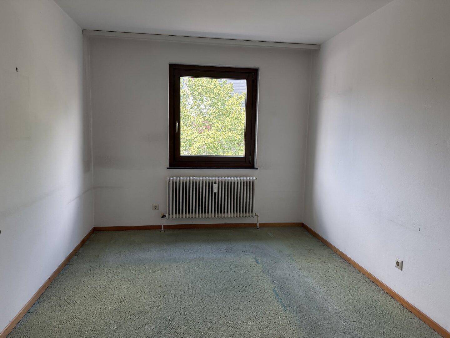 Geräumiges Zimmer mit grünem Teppichboden, Fenster und Heizkörper, bietet vielseitige Nutzungsmöglichkeiten.