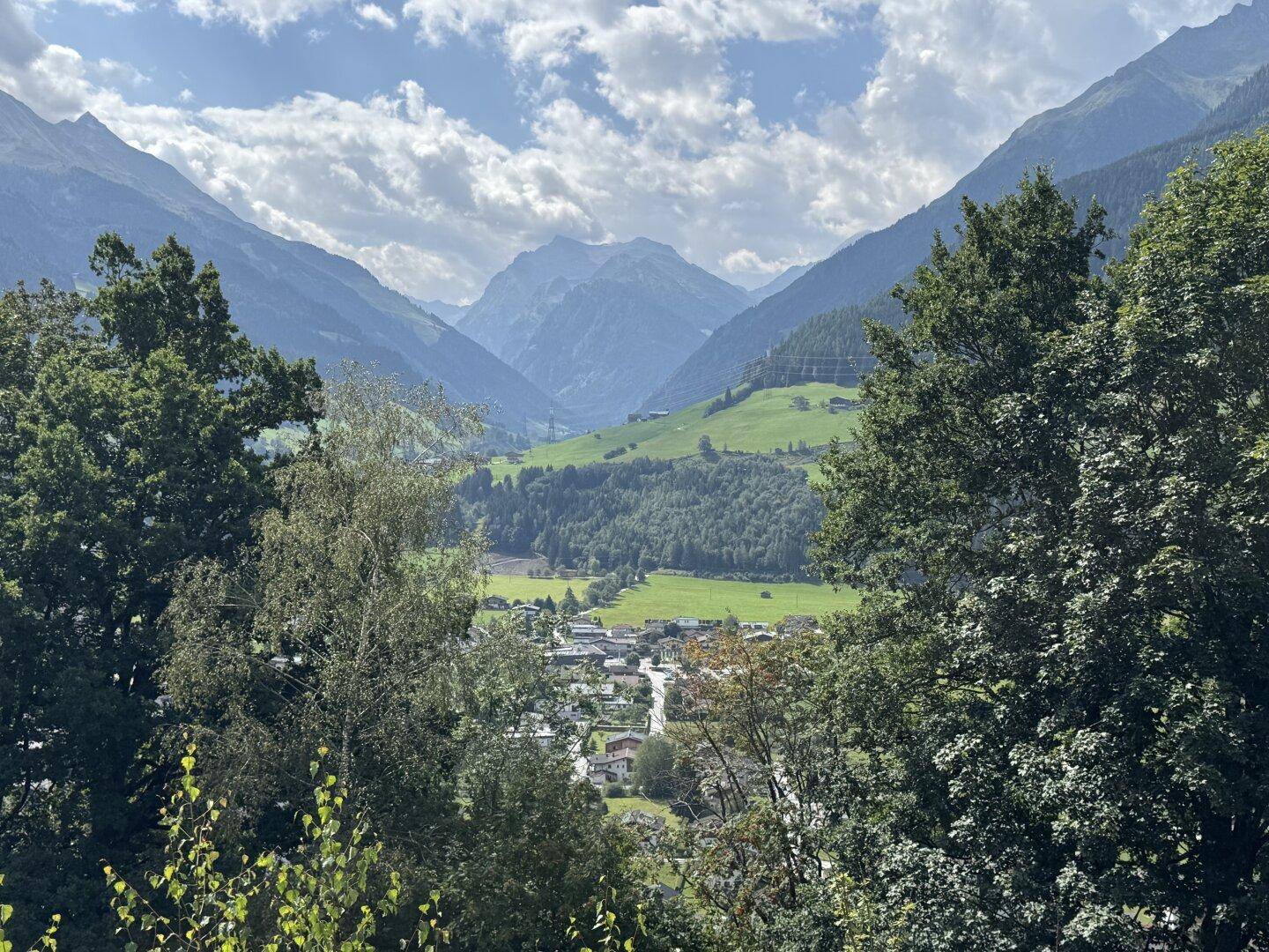 Malerischer Blick auf ein idyllisches Dorf im Tal, umgeben von dichten Bäumen und hohen Bergen.