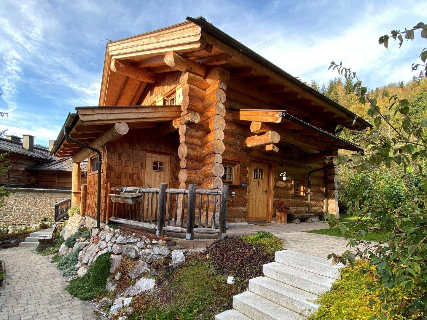 Charmantes Holzhaus mit traditioneller Architektur, umgeben von grüner Landschaft und Bergen.