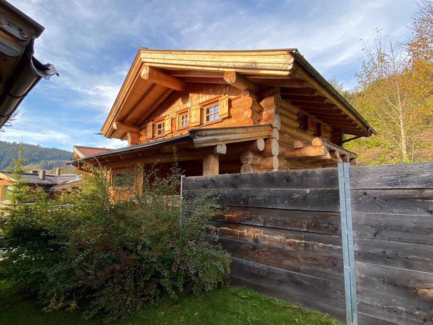 Holzhaus mit traditionellem Design, umgeben von einem Holzzaun und Bäumen.